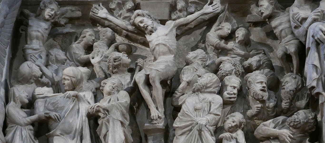 The dead Christ on the cross dominates the deeply carved relief panel. His arms are raised in a V shape and and his ribs protrude. The two thieves are at each side on their crosses. At our left, Mary faints as two women and a grieving St John hold her. Behind her, another woman has her arms outstretched and raised in a dramatic gesture of grief that mirrors Jesus's own posture. In the lower corner at our right, the Jewish elders, with long curly beards, seem to fall away from the cross.