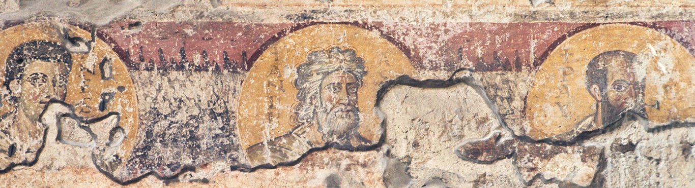 On a wall with peeling plaster, there are three busts of male saints, each within a gold medallion with an inscription identifying them: Sts John, Andrew and Paul. The facial types are typical: John is young and unbearded; Andrew has long, curly, even disheveled, grey hair and a full grey beard; Paul is bald on the crown with dark hair above his ears and extending into a long beard.
